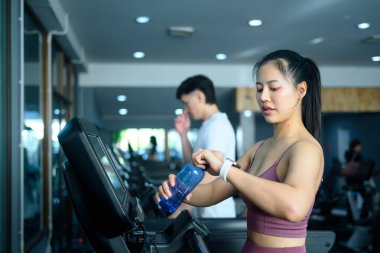 Güzel sporcu kadın koşu bandında egzersiz yapıyor ve akıllı bakışlarını kontrol ediyor..