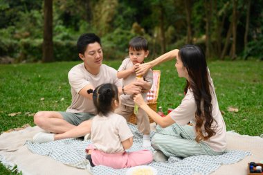 Sevgi dolu aile, yemyeşil bir parkta piknik yapmayı sever. Ebeveynlik, açık hava eğlencesi ve aile bağları..