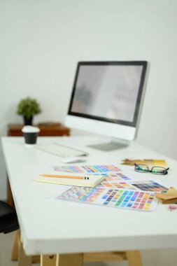 Bilgisayar monitörü, renk örnekleri ve malzeme örnekleriyle yaratıcı tasarımcı çalışma alanı.