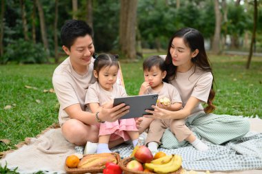 Sıcak ve sevgi dolu bir aile piknikte birlikte vakit geçirir ve dijital tableti eğlence ya da öğrenim için kullanır..