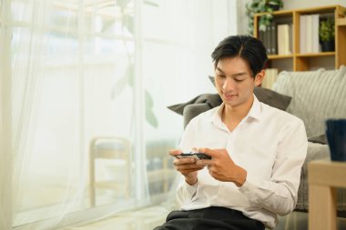 Genç Asyalı adam evde rahatlıyor ve mobil oyun oynuyor..