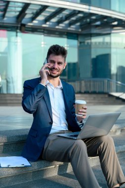 İş adamı, modern bir binanın merdivenlerinde otururken telefonla konuşuyor..