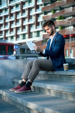 Ofis binasının merdivenlerinde dijital tablet kullanan takım elbiseli profesyonel işadamı..