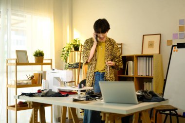 Gülümseyen genç tasarımcı yaratıcı bir moda stüdyosunda telefon görüşmesi yapıyor..