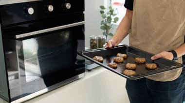 Çikolata parçacıklı kurabiye hamuruyla dolu fırın tepsisini tutan genç adam, pişirmeye hazır..