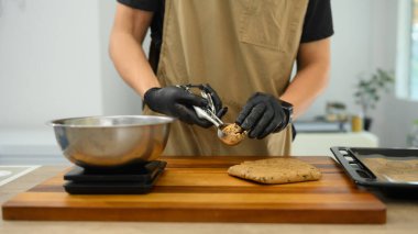 Fırıncı siyah eldiven giyer, çikolata parçacıklı kurabiye hamurunu fırın tepsisine atar..