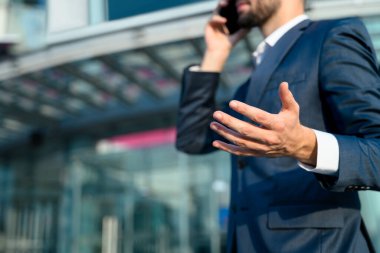 Lacivert takım elbiseli profesyonel işadamı modern bir ofis binasının önünde cep telefonuyla konuşuyor..