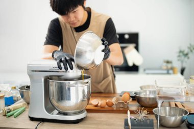 Erkek fırıncı kurabiye hamuru için tezgah karıştırıcısına malzeme ekliyor.