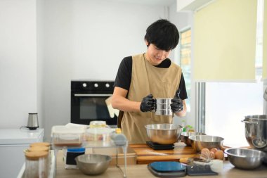 Gülümseyen fırıncı, parlak bir mutfakta kurabiye hamuru için un seçiyor..