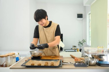 Neşeli genç fırıncı modern bir mutfakta çikolata parçacıklı kurabiyeler hazırlıyor..