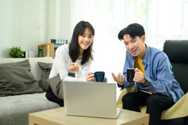 Genç çift kahveyi seviyor ve oturma odalarında dizüstü bilgisayarda geziniyorlar..