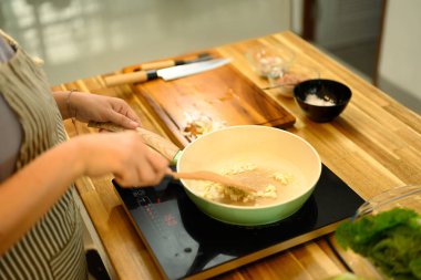 Lezzetli bir yemek hazırlarken kızartma tavasında malzemeleri karıştıran yetişkin bir kadın..