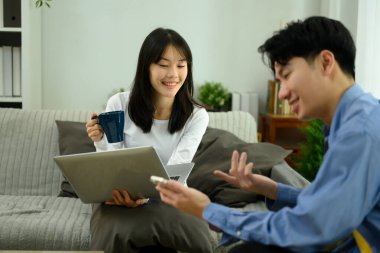 Mutlu genç çift, dizüstü bilgisayar ve akıllı telefon kullanarak kanepede dinleniyor..