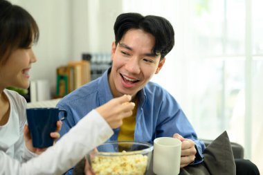 Mutlu genç çift kanepede oturup film izlerken bir kase patlamış mısırlarını paylaşıyorlar..