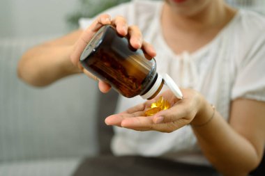 Orta yaşlı bir kadın eline kahverengi bir şişeden balık yağı dolduruyor..