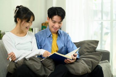 Mutlu Asyalı çift kanepede kitap okuyor ve evde birlikte vakit geçiriyorlar..