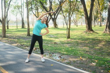 Gülümseyen genç kadın parkta egzersiz yaptıktan sonra vücudunu esnetiyor..