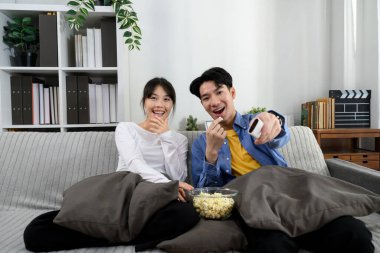 Mutlu genç çift evde televizyon izliyor ve bir kase patlamış mısır paylaşıyor..