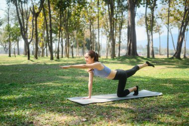 Konsantre genç bayan huzurlu bir parkta Bird Dog Poose yapıyor..