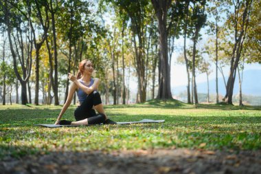 Yoga yapan genç bir kadın. Doğada yoga yapıyor. Balıkların Efendisi pozunda oturuyor..
