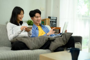 Mutlu çift dizüstü bilgisayarda bir şeyler izleyip kanepede dinleniyor..