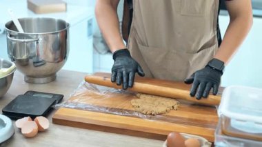 Kurabiye hamuru yuvarlayan siyah eldivenli fırıncı ahşap bir tahta üzerinde merdaneyle.