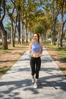 Manzaralı bir parkta koşan gülümseyen genç bir kadının tam boy portresi..