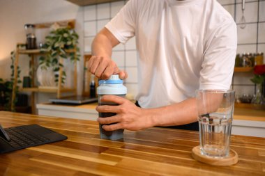 Beyaz spor gömlekli bir adam şık bir mutfakta protein içeceği hazırlıyor..