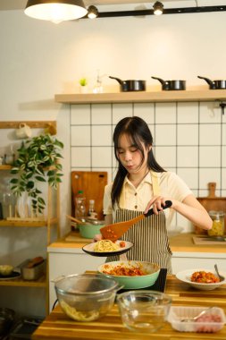 Asyalı bir kadın fırında domates sosu pişirirken taze makarna servis etmeye hazırlanıyor..