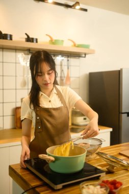 Gülümseyen kadın lezzetli bir ev yemeği hazırlarken haşlanmış spagettiyi buharda pişiren tencereden kaldırıyor..