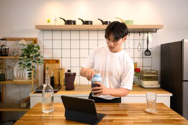 Spor kıyafetli genç adam idmandan sonra ahşap tezgahta protein içeceği hazırlıyor..