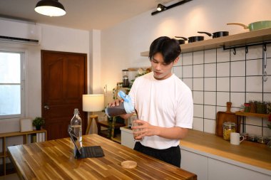 Spor kıyafetli genç adam idmandan sonra ahşap tezgahta protein içeceği hazırlıyor..