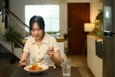 Mutlu genç bayan yemek masasında oturmuş leziz bir tabak spagetti yiyor..