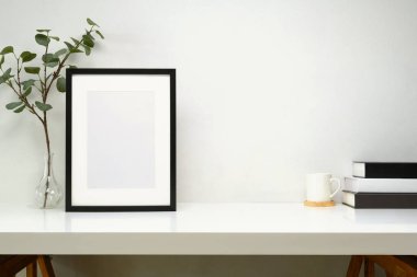 Kitaplı modern çalışma alanı, bir fincan kahve, boş çerçeve ve saksı bitkisi..