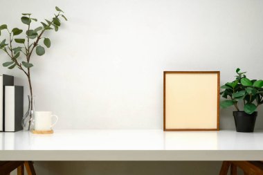 Kitapları, resim çerçevesi, kırtasiyesi ve dekoratif bitkileri olan şık çalışma alanı.