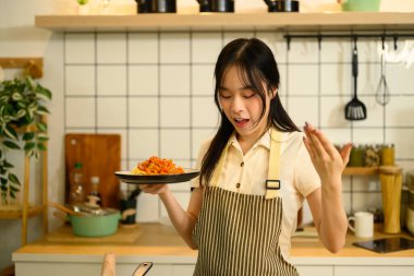 Genç bir kadın mutfağında yeni hazırlanmış bir tabak domates soslu spagetti tutuyor..