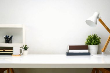 Ahşap lamba, kitaplar ve küçük saksı bitkisi olan minimalist çalışma alanı.
