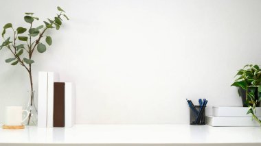 Kitapları, kalem tutacağı ve yeşil bitkileri olan minimalist çalışma alanı.