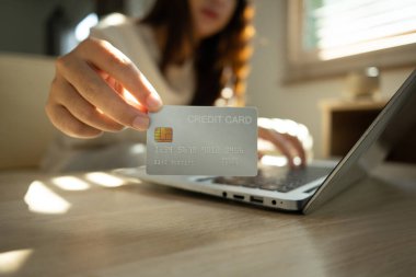 Bilgisayarı, dijital işlemleri ve online alışveriş konseptini kullanırken kredi kartı gösteren bir kadın.