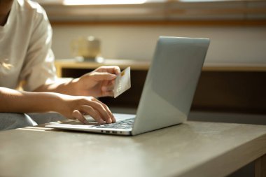 Elinde kredi kartı olan ve evde online alışveriş için dizüstü bilgisayar kullanan bir kadın..