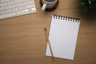 Boş spiral defter, klavye ve kahve ile ahşap masanın en üst görüntüsü..