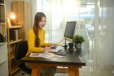 Yaratıcı bir çalışma alanında tasarım projesinde çalışan gülümseyen genç kadın.