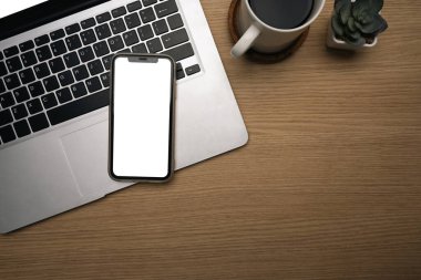 Boş ekranlı akıllı telefon, dizüstü bilgisayar, kahve fincanı ve ahşap masadaki sulu bitki..