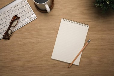 Boş spiral defter, bir fincan sade kahve, gözlük ve tahta masada kablosuz klavye..