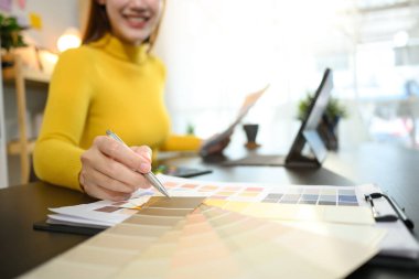 Gülümseyen kadın tasarımcı grafik stüdyosunda tasarım projesi için renk örnekleri seçiyor.