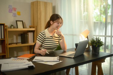 Parlak bir ofiste çalışan gülümseyen bir kadın dizüstü bilgisayar ve belgelerle.
