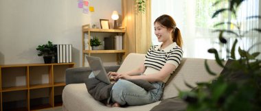 Evde dizüstü bilgisayarıyla çalışan serbest giyinmiş güzel bir kadın..