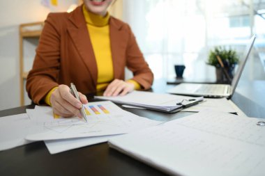 Gülümseyen iş kadını dizüstü bilgisayarla masada oturuyor, grafikleri ve istatistikleri inceliyor..