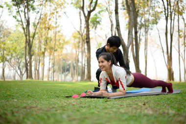 Genç ve güçlü bir kadın antrenör yardımıyla dışarıda poz veriyor..