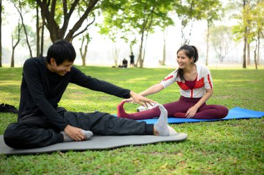 Yeşil bir parkta yoga minderleri üzerinde esneyen neşeli genç bir çift. Sağlıklı yaşam tarzı kavramı.